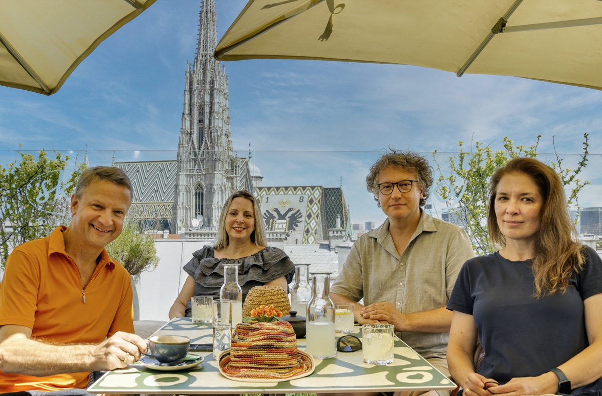 Die vier Wunderwien-Guides an einem Tisch über den Dächern Wiens, hinter ihnen der Stephansdom